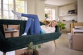 Woman Relaxing On Sofa Using Mobile Phone Surrounded By Unpacking Boxes After Moving Into New Home Royalty Free Stock Photo