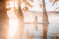 Woman relax on staand up paddle board at quiet lake with morning fog and fall Taxodium distichum trees Royalty Free Stock Photo