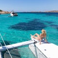 Woman relaxing on a summer sailing cruise, sitting on a luxury catamaran near picture perfect white sandy beach on Royalty Free Stock Photo