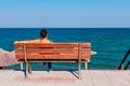 Woman is relaxing on the wooden bench next to the coastline, sea