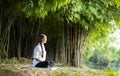 Woman relaxingly practicing meditation in the bamboo forest to attain happiness from inner peace wisdom for healthy mind and soul