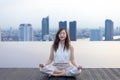 Woman relaxingly practicing meditation at the swimming pool rooftop with the view of urban skyline building to attain happiness