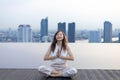 Woman relaxingly practicing meditation at the swimming pool rooftop with the view of urban skyline building to attain happiness