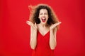 Woman releasing stress screaming out loud. Expressive and over-emotive attractive curly-haired woman in elegant red