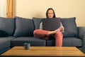 Woman at remote work sits cross leg on a sofa smiles and typing on a laptop