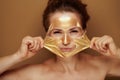 Woman removing golden mask on brown background