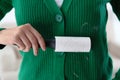 Woman removing hair from green knitted jacket with lint roller on light background, closeup Royalty Free Stock Photo