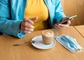 Woman removing the mask, drinking coffee and chating in the cafe during lockdown