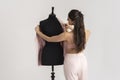 Woman removing pink jacket from tailors dummy to place on hanger.