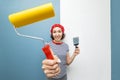 Woman repairman poses with a roller and trowel against the background of pasted wallpaper and a plastered wall