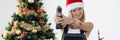 Woman repairman in santa hat holding electric drill near christmas tree