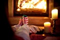 Woman resting her legs in striped festive socks in a room with a burning fireplace and candles on cozy Christmas evening Royalty Free Stock Photo