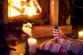 Woman resting her legs in striped festive socks in a room with a burning fireplace and candles on cozy Christmas evening Royalty Free Stock Photo