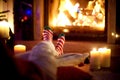 Woman resting her legs in striped festive socks in a room with a burning fireplace and candles on cozy Christmas evening Royalty Free Stock Photo