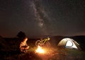 Woman resting at night camping near campfire, tourist tent, bicycle under evening sky full of stars Royalty Free Stock Photo