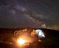 Woman resting at night camping near campfire, tourist tent, bicycle under evening sky full of stars Royalty Free Stock Photo