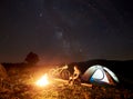 Woman resting at night camping near campfire, tourist tent, bicycle under evening sky full of stars Royalty Free Stock Photo