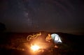 Woman resting at night camping near campfire, tourist tent, bicycle under evening sky full of stars Royalty Free Stock Photo