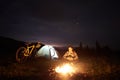 Woman resting at night camping near campfire, tourist tent, bicycle under evening sky full of stars Royalty Free Stock Photo