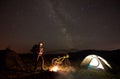 Woman resting at night camping near campfire, tourist tent, bicycle under evening sky full of stars Royalty Free Stock Photo