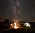 Woman resting at night camping near campfire, tourist tent, bicycle under evening sky full of stars Royalty Free Stock Photo