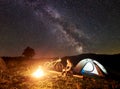 Woman resting at night camping near campfire, tourist tent, bicycle under evening sky full of stars Royalty Free Stock Photo