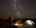 Woman resting at night camping near campfire, tourist tent, bicycle under evening sky full of stars Royalty Free Stock Photo