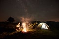 Woman resting at night camping near campfire, tourist tent, bicycle under evening sky full of stars Royalty Free Stock Photo