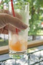 Woman resting sitting on the balcony with openwork metal bars, holding a misted glass with a cold summer drink and a straw