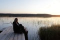 Woman resting on wooden bridge by lake at sunset Royalty Free Stock Photo