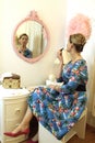 Woman in a retro dress and heels looking at reflection at vanity preparing to put on lipstick Royalty Free Stock Photo