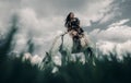 Woman rides on horseback in image of warrior amazon on grass and sky background