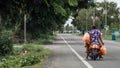 Woman riding on back of motorcycle holding plastic bags full of fruit