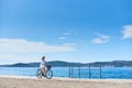 Woman riding a bicycle along stony sidewalk on blue sparkling sea water