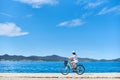 Woman riding a bicycle along stony sidewalk on blue sparkling sea water