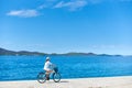 Woman riding a bicycle along stony sidewalk on blue sparkling sea water