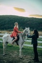 Woman riding grey arabian horse in pink dress. Handsome bearded man driving horse for a bridle and looking at his Royalty Free Stock Photo