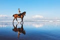 Woman riding horse on beach along sea by water pool