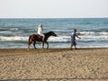 Woman riding a horse with hijab by the beach. Muslim woman sitting on horseback, a horse man directs beside the Caspian Sea