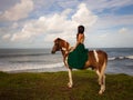 Woman riding horse near the ocean. Outdoor activities. Asia woman wearing long green dress. Traveling concept. Cloudy sky. View Royalty Free Stock Photo