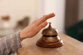 Woman ringing hotel service bell at wooden reception desk, closeup Royalty Free Stock Photo