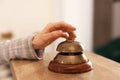 Woman ringing hotel service bell at wooden reception desk, closeup Royalty Free Stock Photo