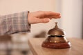 Woman ringing hotel service bell at wooden reception desk, closeup Royalty Free Stock Photo