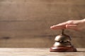 Woman ringing hotel service bell at wooden table, closeup. Space for text