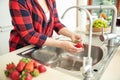 Woman rinses the strawberries in the kitchen