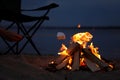 Woman roasting marshmallow over burning firewood on beach, closeup