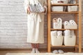 Woman in robe standing and holding white wire basket of folded bed sheets near bathroom linen closet