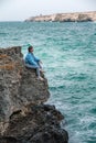 Woman rocks sea. A woman in a blue jacket sits on a rock above a rock above the sea and looks at the raging ocean. Girl Royalty Free Stock Photo