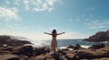 A woman on the rocky beach with her arms wide, taking in the fresh air and the wind