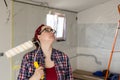 A woman with a roller in hands looks up while examining a surface for painting. Royalty Free Stock Photo